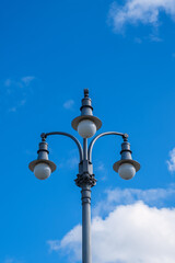 Fototapeta na wymiar An old street light against a blue sky with white clouds