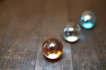 Gro&szlig;e und gl&auml;nzende Glaskugeln in verschiedener Anzahl auf einem braunen Holztisch. Sie repr&auml;sentieren die vier oder f&uuml;nf Elemente.