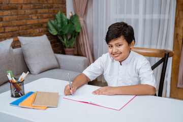 Smiling boy writing in a book while doing studying in the room at home