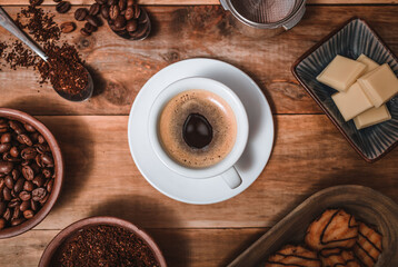 cup of espresso, accompanied by beans and ground coffee, cookies with chocolate and white chocolate, on rustic wooden background and top view