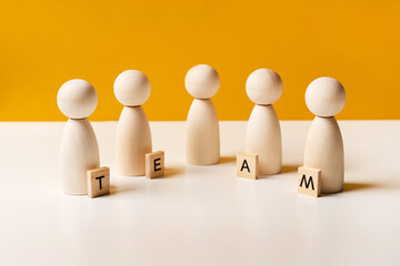 Company of wooden people on a yellow background with letters. The concept of team work and management, copy space