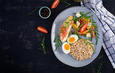 Breakfast oatmeal porridge with boiled egg, salmon sandwich and tomatoes salad. Healthy food. Top view, overhead,  copy space