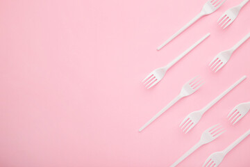 Many plastic forks on a pink background.