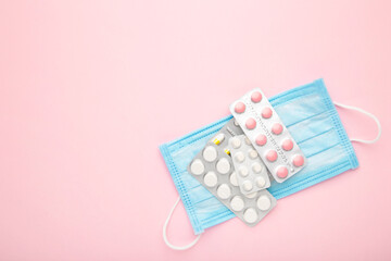 Medical face mask and pills on pink table background. Coronavirus COVID-19 concept.