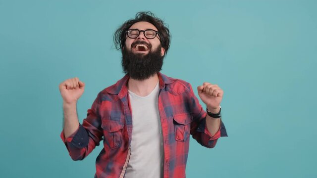 Close up of an young bearded man dancing and posing over turquoise background. Good mood.