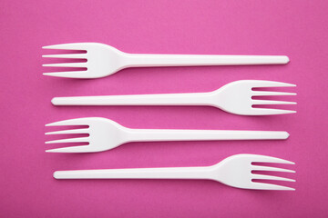 Many plastic forks on a pink background.