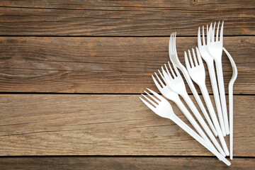 Many white plastic forks on a grey wooden background.