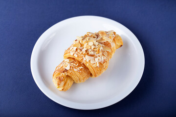 Fresh croissant with almonds on a white plate.