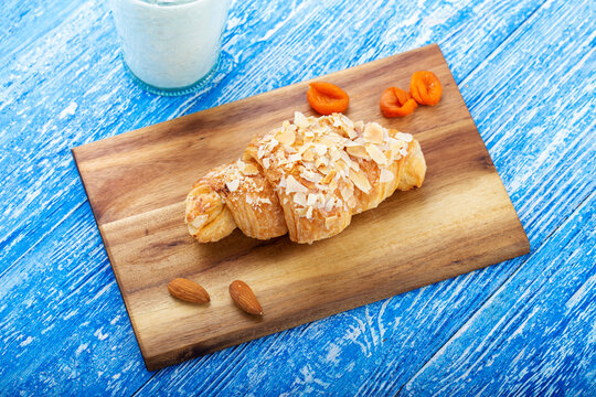 Fresh croissant with almonds on a wooden plank.
