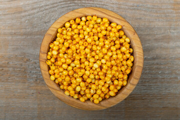 Sea buckthorn in a wooden bowl on a wooden table.