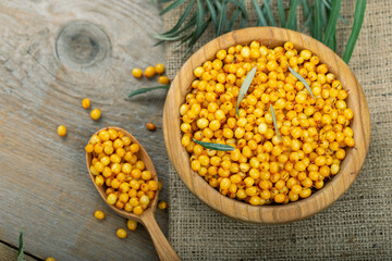 Sea buckthorn with leaves in a wooden bowl on a wooden table.