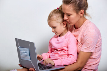 Fototapeta na wymiar Virus protection concept. Closeup portrait of сute girl 4-5 year old and her mother in pink clothes, showing laptop which medical mask on screen, gray background