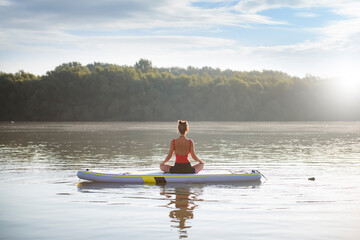 Woman meditating and practicing yoga during sunrise in paddle board