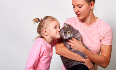 Happy mother with her daughter is holding cat on gray background