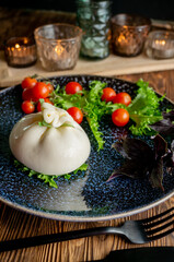 Traditional Italian dish of burrata Stratocell. Burrata on a dark plate is served for a romantic dinner with tomatoes and arugula