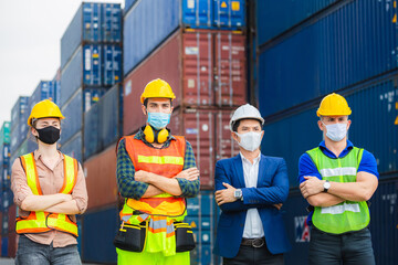 Factory worker and engineer team wearing protection face mask against coronavirus ( COVID-19 ) with arms crossed at cargo containers