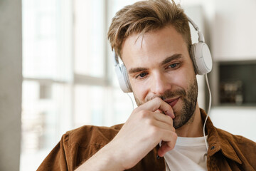 Naklejka premium Handsome happy guy smiling while listening music with headphones