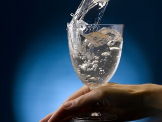 Water splashing into glass. Hand holds the stem.