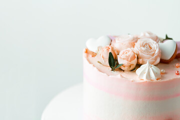 Pink cake decorated with pink rose flowers and merengue cookies on the white background