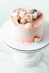 Pink cake decorated with pink rose flowers and merengue cookies on the white background