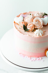 Pink cake decorated with pink rose flowers and merengue cookies on the white background