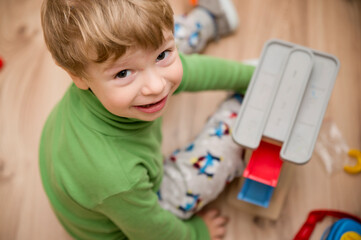 charming boy plays on the floor with car track. look at lense. baby games. toddler activities. Kindergarten boy at home during quarantine. happy 3 - year kid.