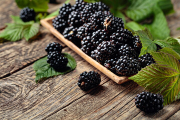 Ripe juicy blackberries with leaves on a wooden table.