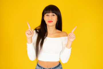 Portrait of a happy young woman dressed in casual clothes pointing fingers up at copy space isolated over yellow background
