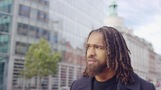 Handsome black male with stylish dreadlocks walks through the city, in slow motion