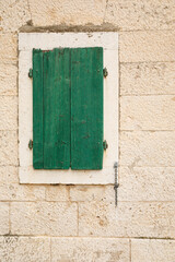 Vintage green window with shutters on stone wall.