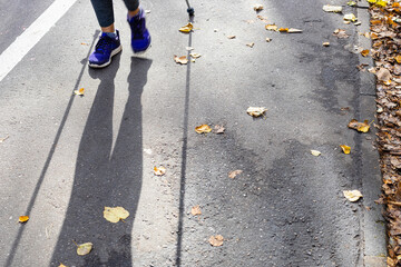 legs and shadow of walker of Nordic walking on pathway in city park on sunny autumn day