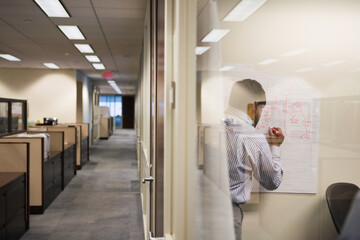 Businessman writing on white board seen through glass wall at office