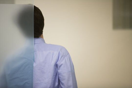 Rear View Of Businessman Standing Behind Glass Wall At Office