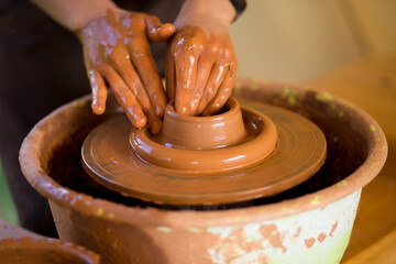 Hands of potte makes pottery dishes on potter's wheel. Sculptor in workshop makes clay product