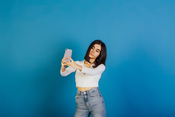 Serious confident woman are taking a selfie isolated on a blue background. She wear stylish trendy clothes. Copy space.