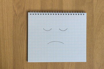 student notebook with sad smile on wooden background