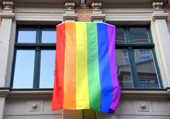 Zwischen zwei Fenstern hängende Regenbogen-Fahne 
