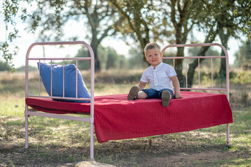 Cute small boy sitting on outdoor bed