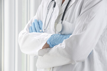 Close up image of medical worker wearing protective surgical mask and rubber gloves with crossed arms.
