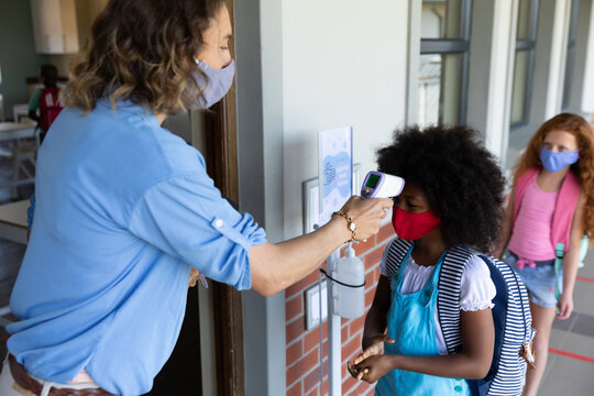 Female teacher wearing a face mask measuring temperature of a girl - Powered by Adobe