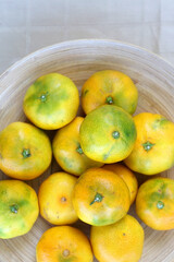 Wooden bowl full of tangerines on a table. Top view.