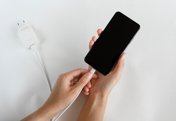 Charging a smartphone via a USB cable and a power supply on a white background, top view. Silhouette of a black smartphone hanging with a usb charging cable on a white background. 
