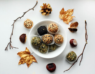 Fototapeta na wymiar natural hand made sweets in a bowl decorated with golden marple leaves, chestnuts, cones and branches. Healthy dessert.
