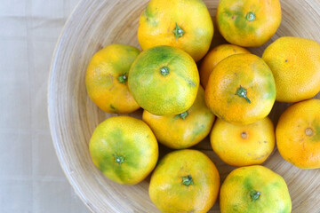 Wooden bowl full of tangerines on a table. Top view.