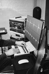 black and white male music producer hands tweaking midi keyboard knob for editing waveform on computer monitor in home studio