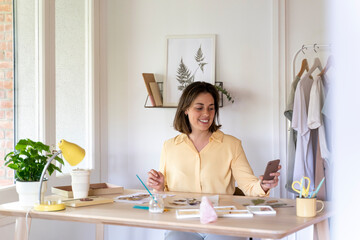 Smiling beautiful young woman using smart phone while sitting at home