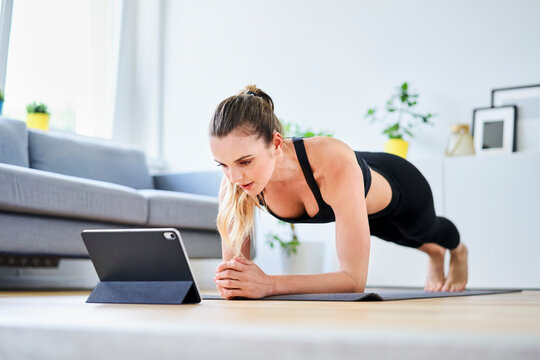 Woman learning plank exercise on internet through digital tablet at home