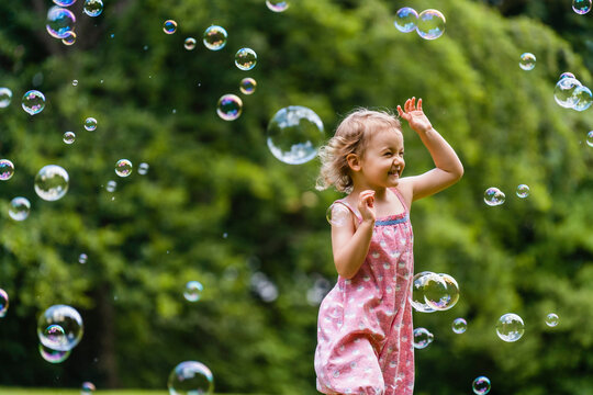 Cheerful girl running amidst bubbles at park