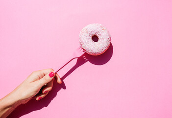 Hand of woman holding fork with sweet doughnut