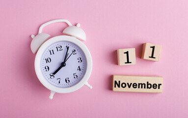 November 11 is written on wooden cubes near a white alarm clock on a pink background. Singles Day. Mega sales day.